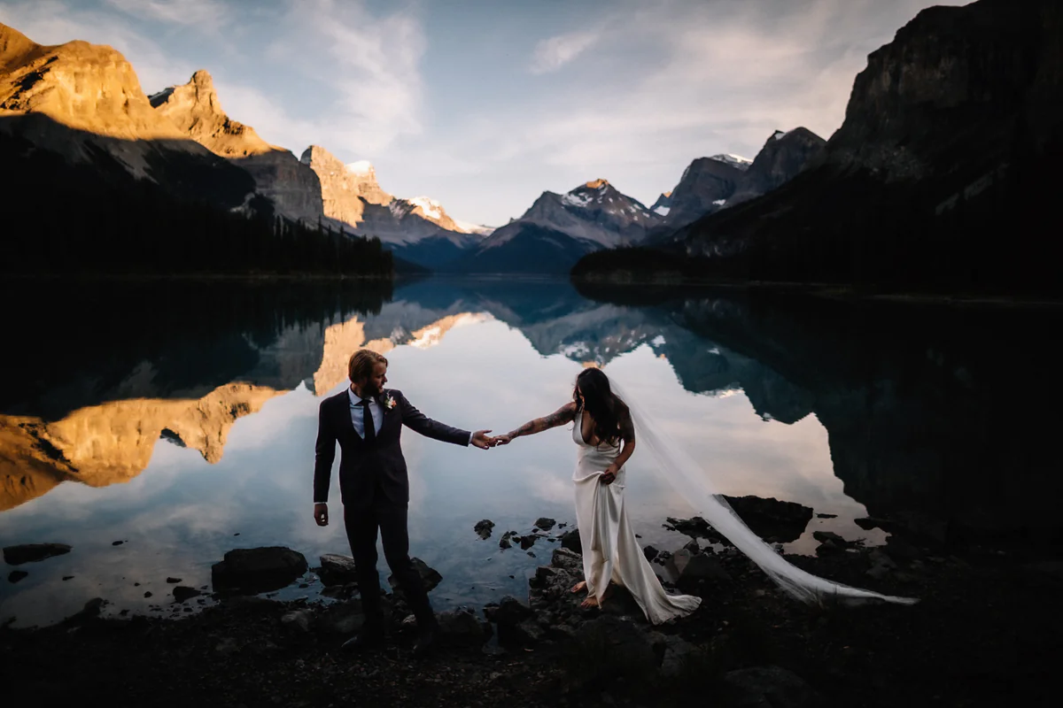 Un couple sur une rive rocheuse, les montagnes déchiquetées se reflétant dans l'eau au crépuscule (Version finale de Gabe)