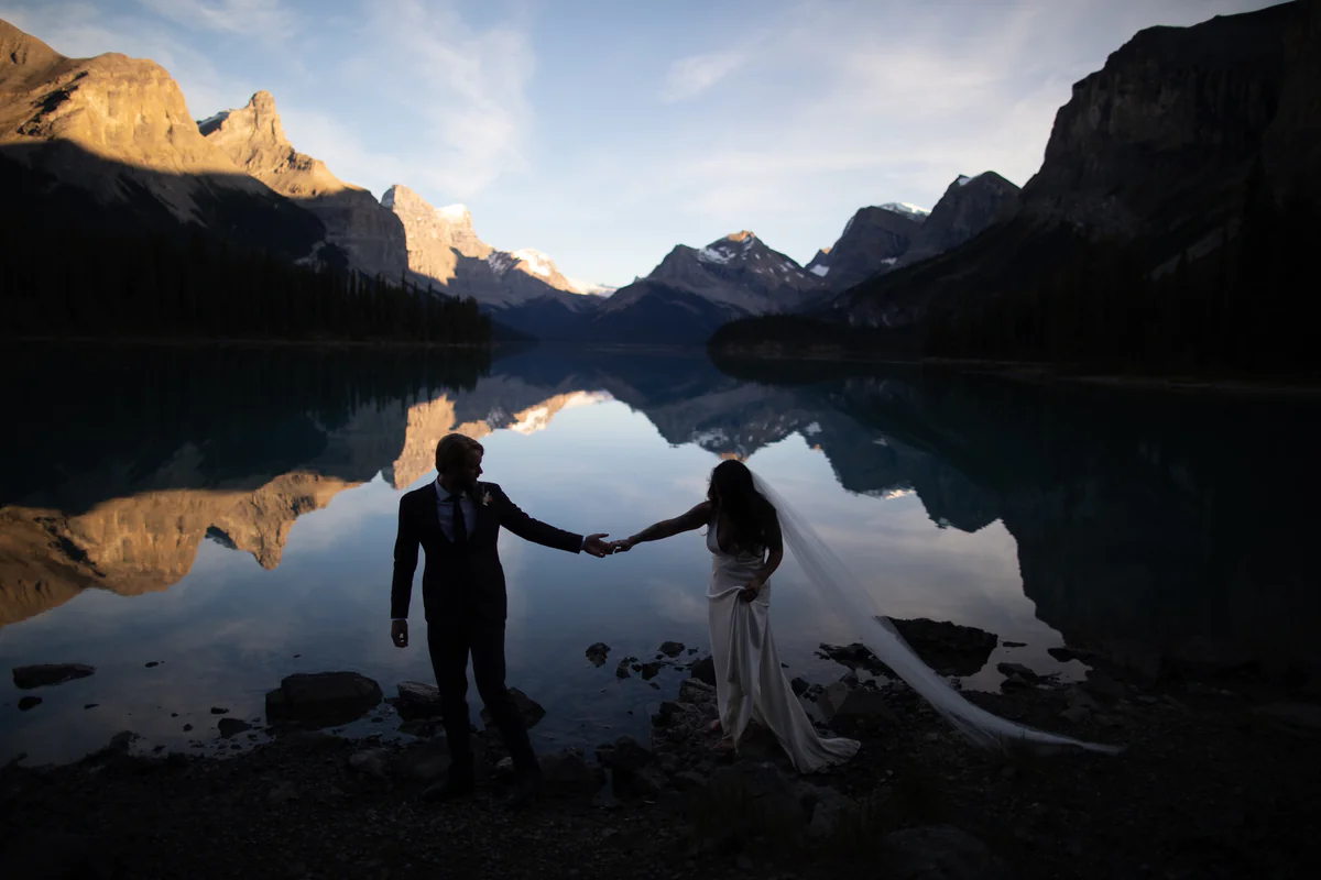 Un couple sur une rive rocheuse, les montagnes déchiquetées se reflétant dans l'eau au crépuscule (Originale)