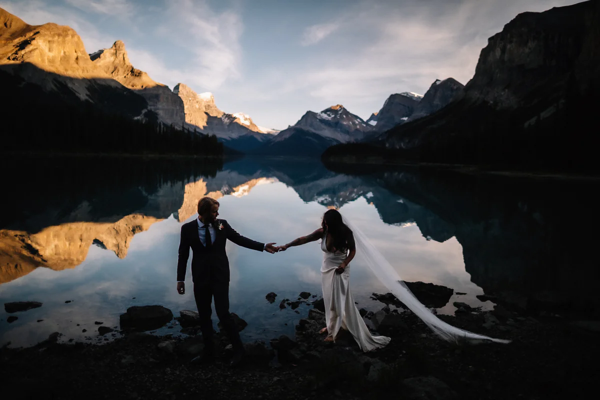 Un couple sur une rive rocheuse, les montagnes déchiquetées se reflétant dans l'eau au crépuscule (Retouche PHAiTO)