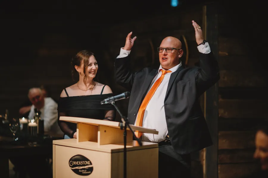 Un invité lève les bras en plein discours, derrière un pupitre éclairé à la chandelle
