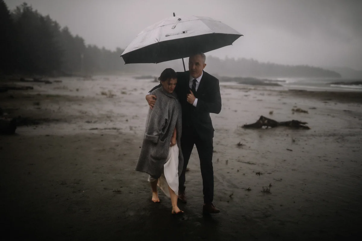 Un couple s'abrite sous un grand parapluie sur une plage brumeuse, sous la pluie (Version finale de Gabe)