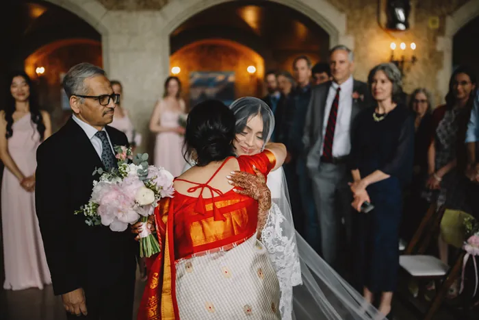 La mariée, voilée, enlace sa mère vêtue d'un sari rouge et blanc au début de la cérémonie