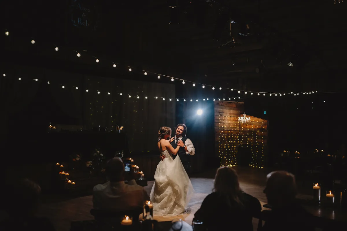 Première danse du couple sous des guirlandes lumineuses, dans une salle sombre (Retouche PHAiTO)