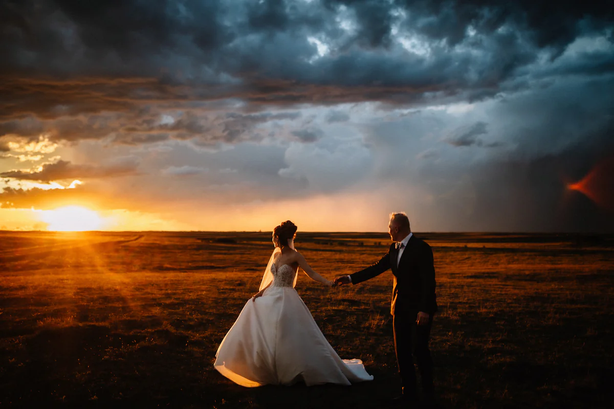 Un couple se tient par la main dans une plaine ouverte alors que le soleil perce sous les nuages d'orage (Version finale de Gabe)