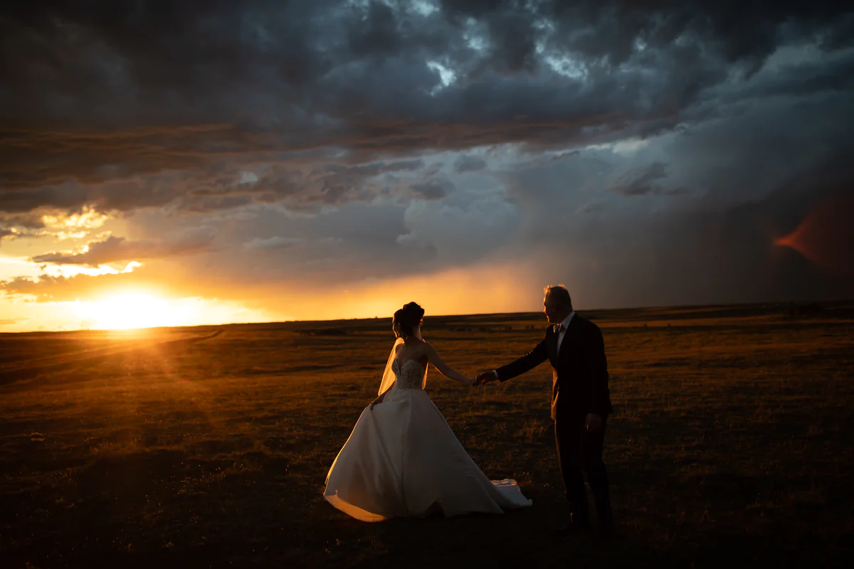 Un couple se tient par la main dans une plaine ouverte alors que le soleil perce sous les nuages d'orage (Originale)