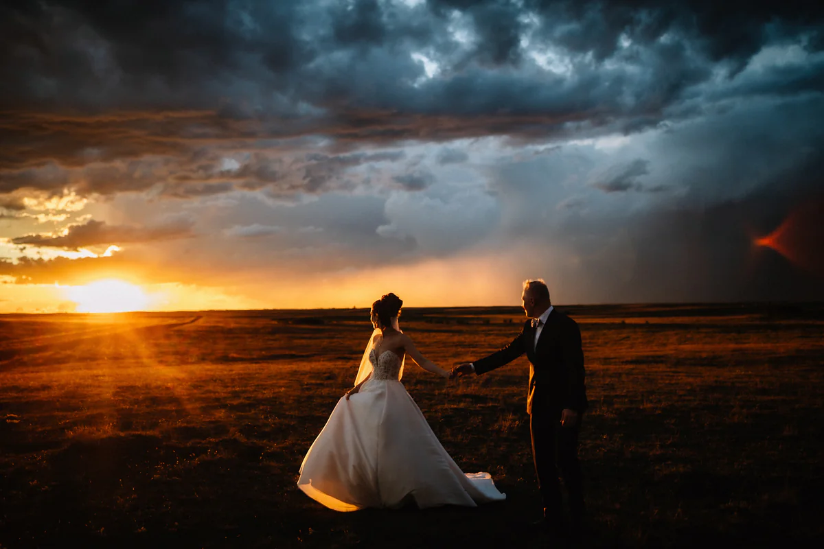 Un couple se tient par la main dans une plaine ouverte alors que le soleil perce sous les nuages d'orage (Retouche PHAiTO)