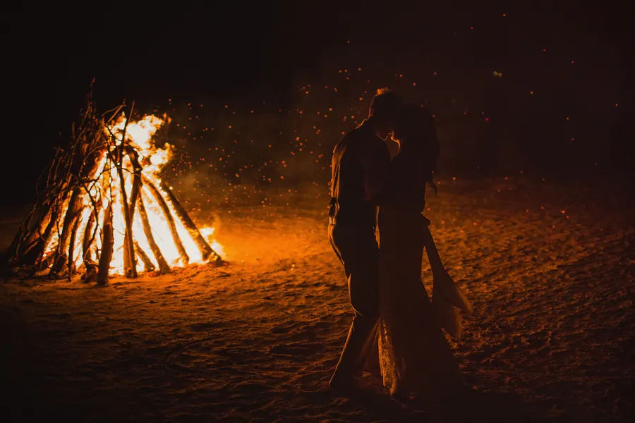 Silhouette d'un couple devant un grand feu de plage, la nuit