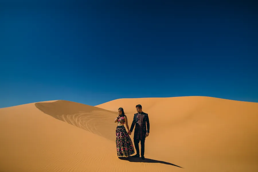 Couple debout sur une dune de sable doré, sous un ciel d'un bleu profond