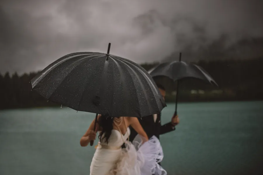 Couple abrité sous des parapluies, sous la pluie, au bord d'un lac gris
