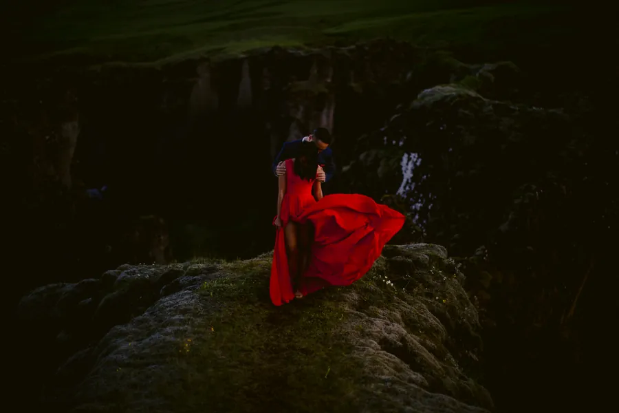 Femme en robe rouge flottante au sommet d'une falaise moussue
