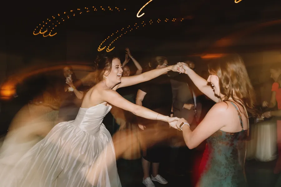 La mariée tourne avec une amie sur la piste de danse, entourée de traînées lumineuses floues