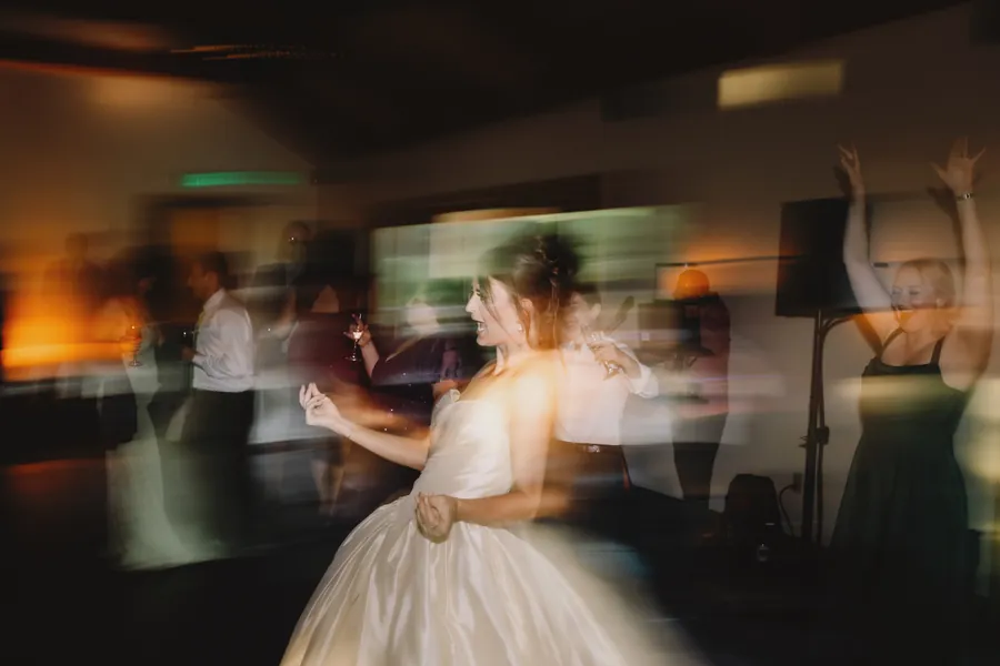 La mariée danse parmi des invités flous, sous des lumières de couleurs mêlées