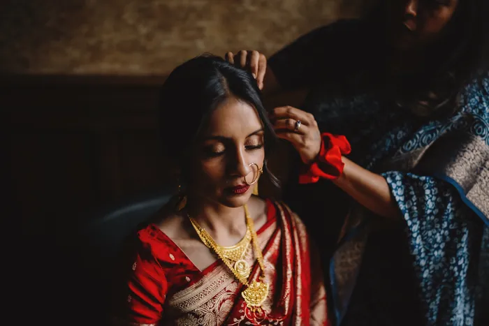 Mariée en sari rouge et bijoux dorés, coiffée par une proche