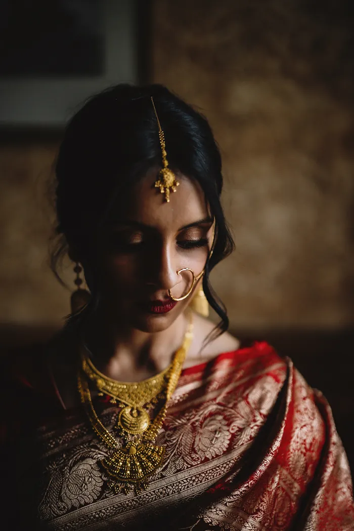 Mariée en sari rouge et or, avec collier en or et anneau de nez, doucement éclairée de côté