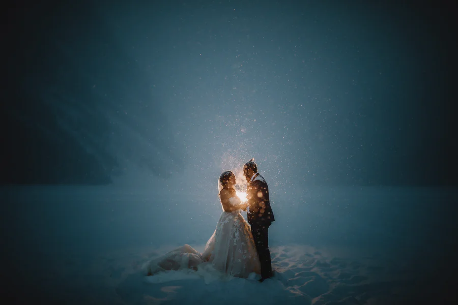 Un couple dans la neige profonde, la nuit, souligné par une lumière vive derrière eux