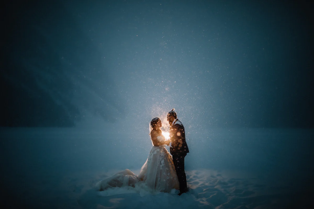 Un couple serré l'un contre l'autre sous la neige qui tombe, éclairé à contre-jour par une lueur vive (Version finale de Gabe)