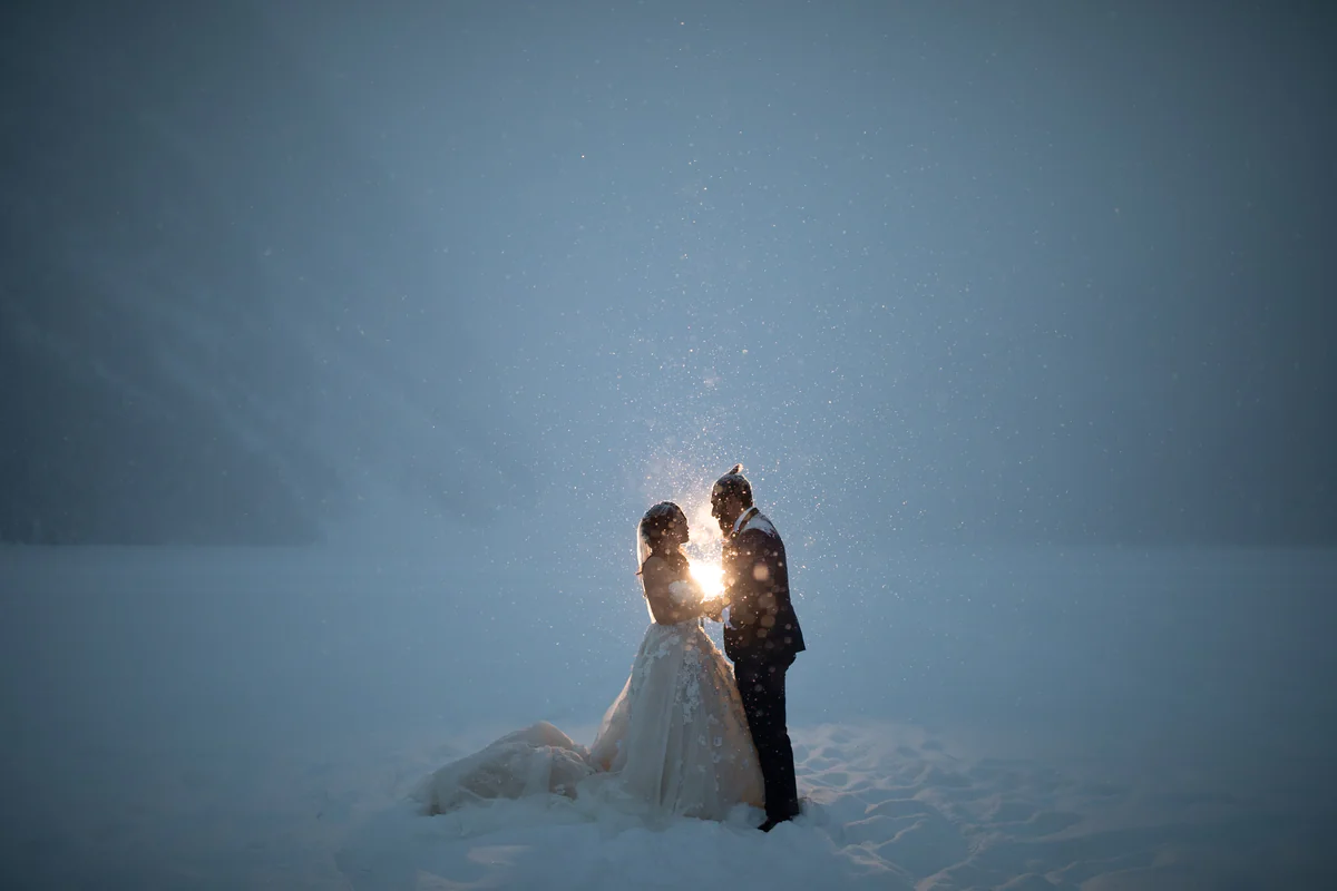 Un couple serré l'un contre l'autre sous la neige qui tombe, éclairé à contre-jour par une lueur vive (Originale)