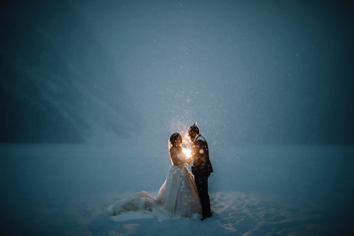 Un couple serré l'un contre l'autre sous la neige qui tombe, éclairé à contre-jour par une lueur vive (Retouche PHAiTO)