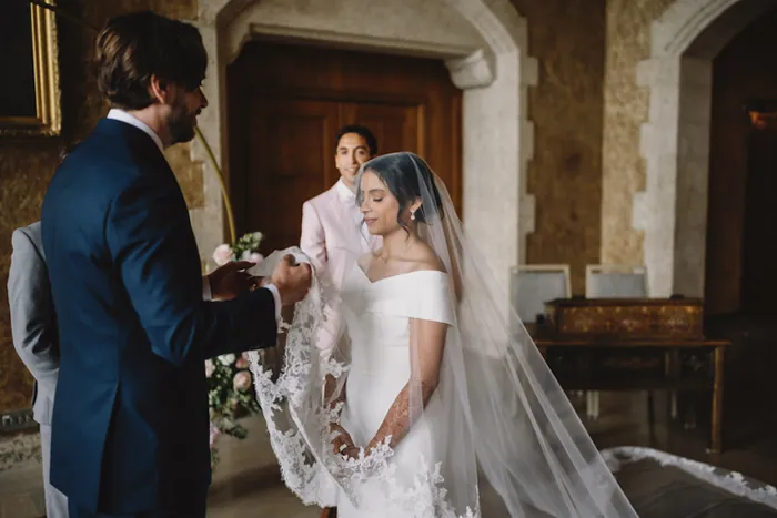 Le marié soulève le voile de dentelle de la mariée à l'autel, sous le regard de l'officiant