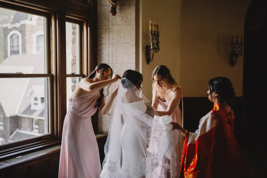 Des demoiselles d'honneur ajustent le voile de la mariée près d'une fenêtre lumineuse
